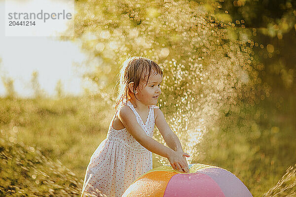 Cute girl playing with colorful ball splashing water at garden