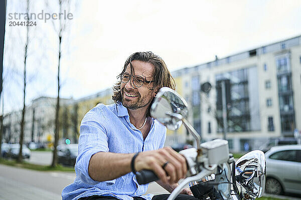 Smiling mature man riding motor scooter in city