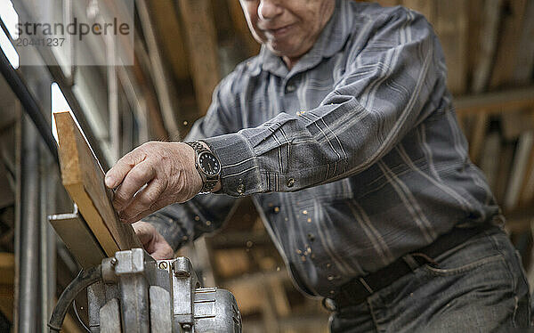 Senior man processing wooden plank on machine in workshop