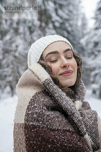 Woman with eyes closed wrapped in blanket at forest