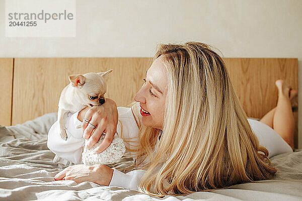 Woman with blond hair playing with dog in bed at home