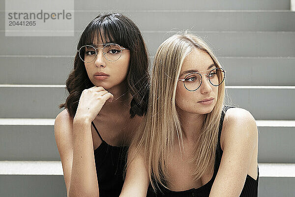 Female friends wearing eyeglasses sitting on steps