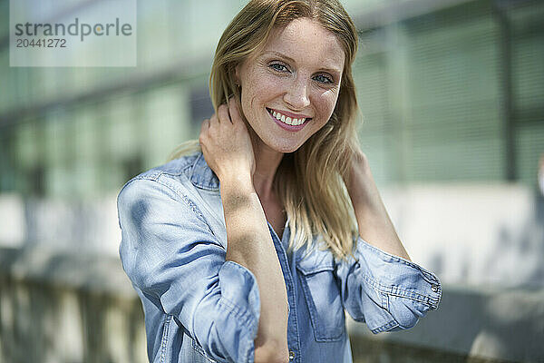 Smiling woman with hands in hair and wearing denim shirt