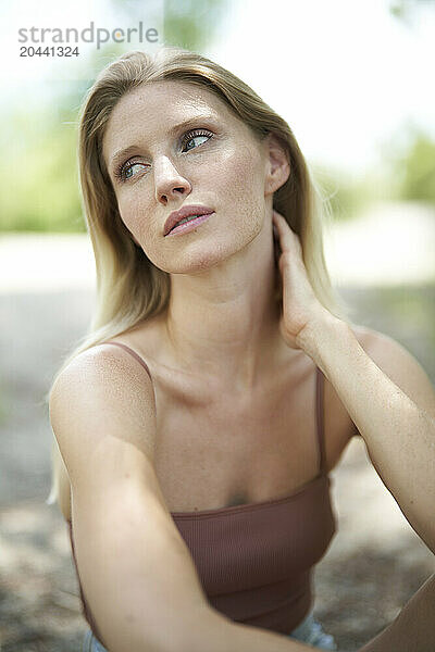 Thoughtful blond hair woman wearing sleeveless top at forest