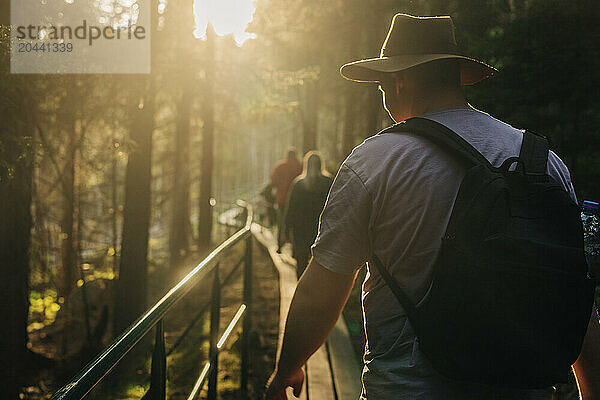 Man with backpack walking on footbridge in forest at sunset