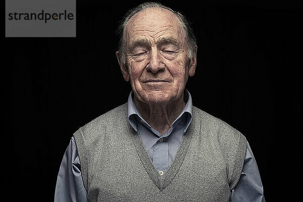 Senior man with eyes closed against black background