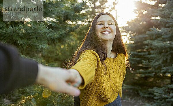 Happy young woman holding hands with man in fir forest