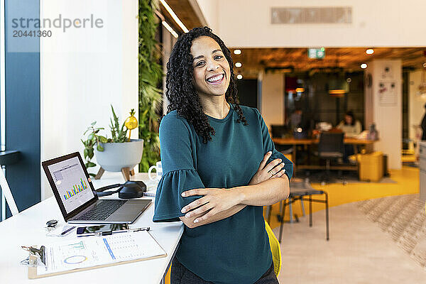 Smiling businesswoman standing with arms crossed at office