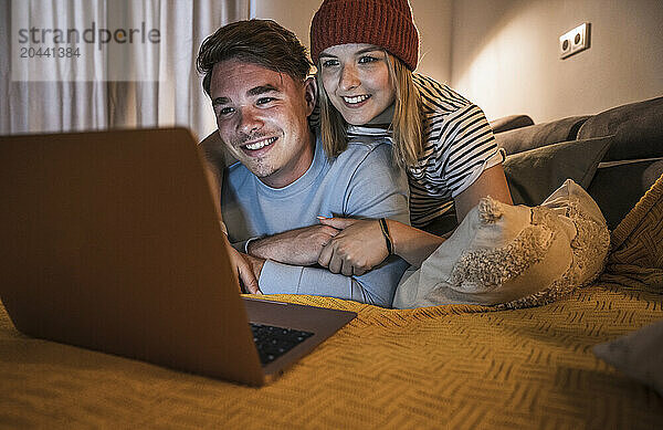 Happy young woman and man using laptop on sofa at home