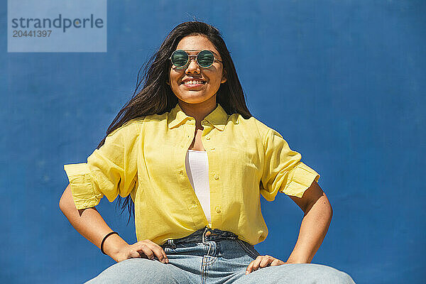 Smiling woman wearing sunglasses in front of wall