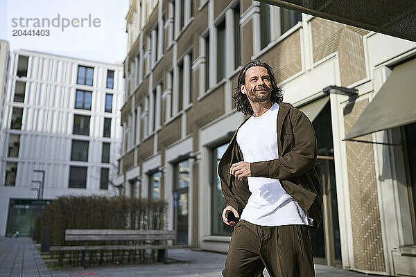 Smiling mature man running in front of modern building on sunny day