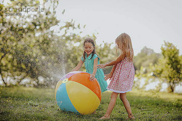 Happy girls playing with colorful ball splashing water at garden