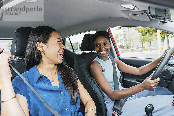 Happy young woman driving car sitting with friend