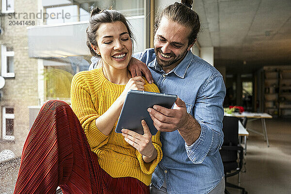 Happy young man and woman watching tablet PC together near window at home