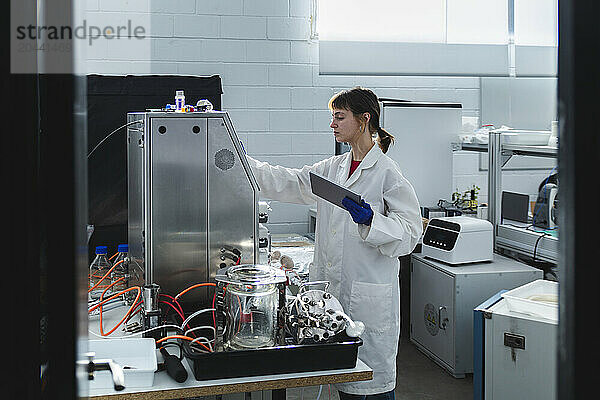 Scientist using tablet PC examining bioreactor in bio laboratory