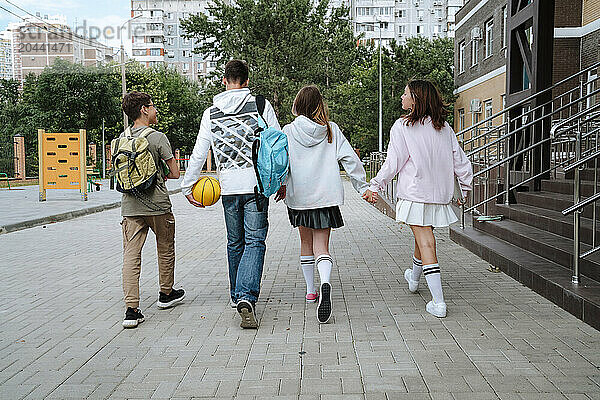 Teenage boys and girls walking side by side at schoolyard