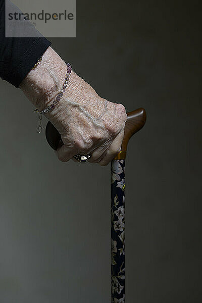 Hand of senior woman holding walking cane against black background