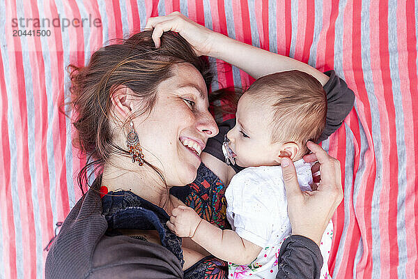 Happy mother lying down and embracing newborn baby at garden