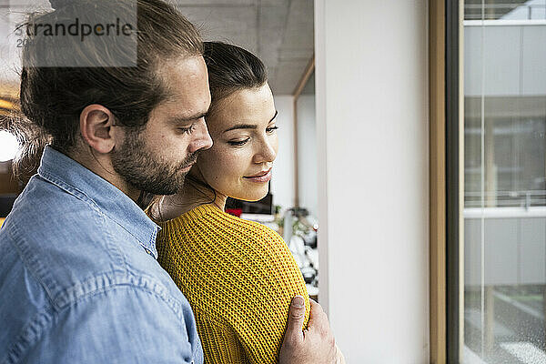 Affectionate young couple embracing near window at home