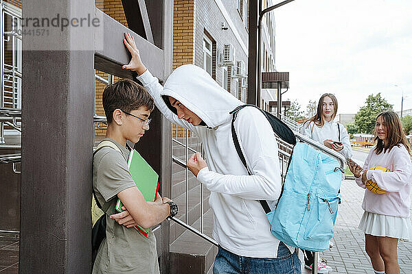 Teenage boy bullying student with girls standing at schoolyard