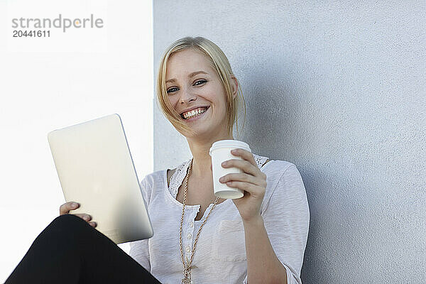 Happy young woman sitting with tablet PC and coffee cup