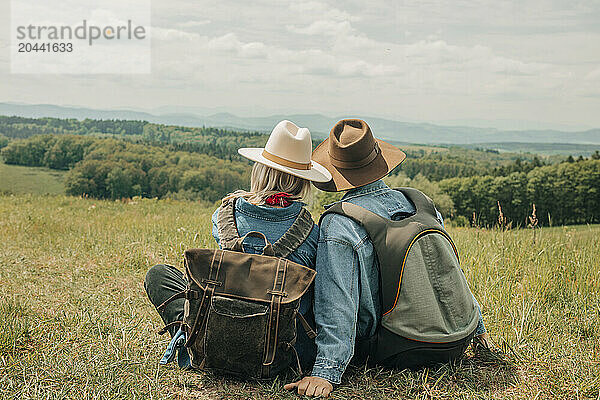 Couple with backpacks sitting on meadow