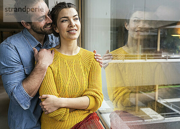 Smiling young girlfriend and boyfriend by window at home