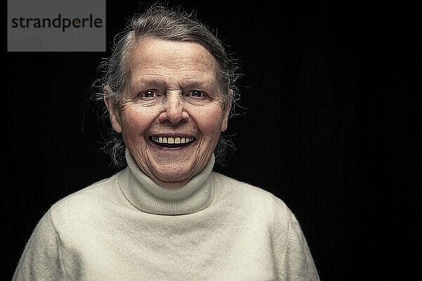 Senior woman laughing against black background