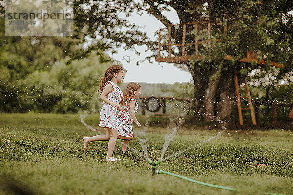 Sisters running near garden hose splashing water on grass