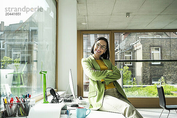 Happy businesswoman sitting with arms crossed on desk day dreaming in office