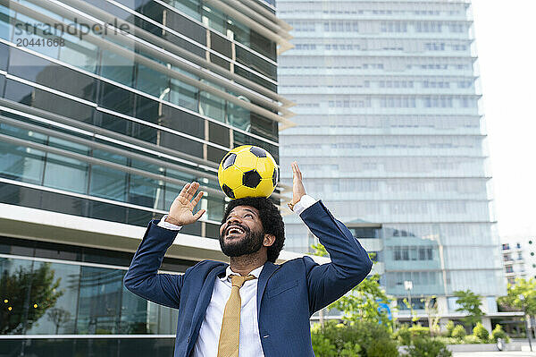 Young businessman balancing soccer ball on head in office park