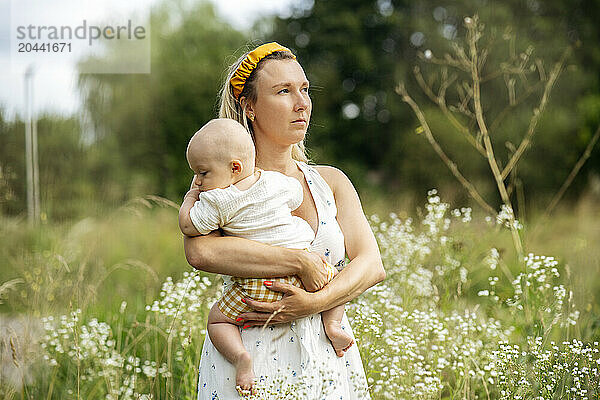 Mother holding baby boy contemplating in garden