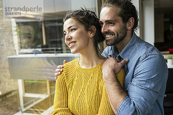 Smiling couple day dreaming together and looking through window at home