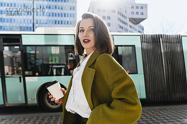 Confident businesswoman with disposable coffee cup in city