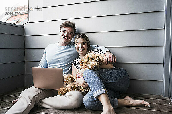 Happy couple sitting with dog in front of wall