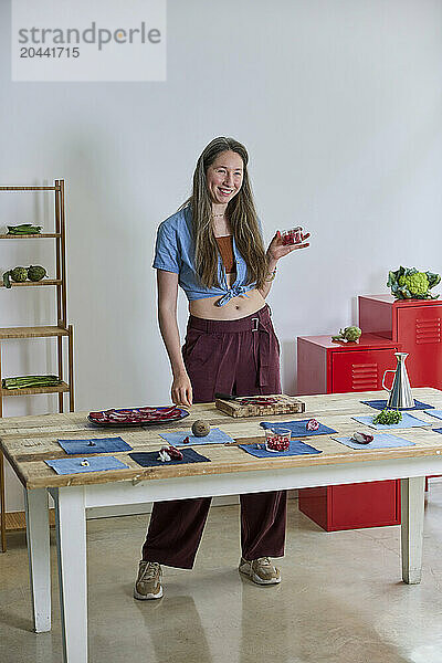 Smiling woman standing by table with variation of food at kitchen