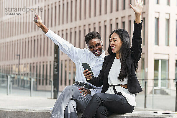 Cheerful multiracial businesswomen sharing smart phone sitting at office park