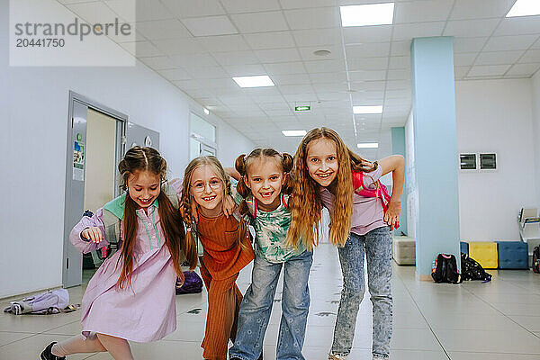 Carefree schoolgirls with arm around standing in school corridor