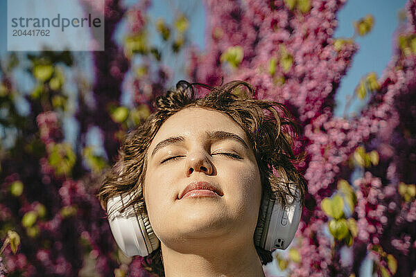 Woman with eyes closed listening to music through wireless headphones