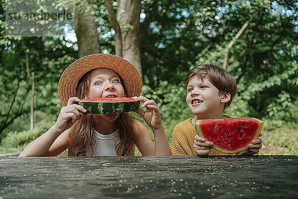 Boy and girl enjoy eating watermelon on table during summer