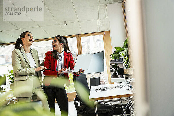 Laughing businesswoman using laptop with coworker at office