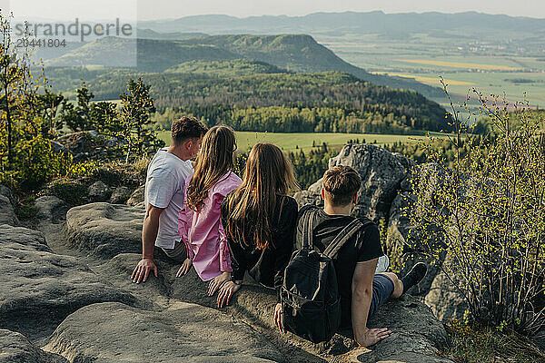 Happy couples sitting on rock and looking at mountains