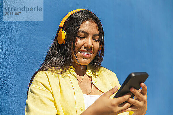 Young woman using smart phone in front of wall