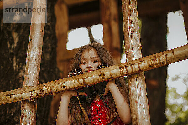 Smiling girl with binoculars sitting at tree house