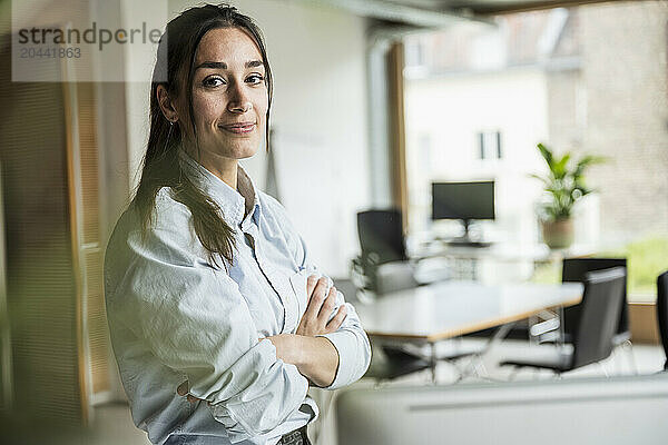 Young businesswoman with arms crossed standing at office