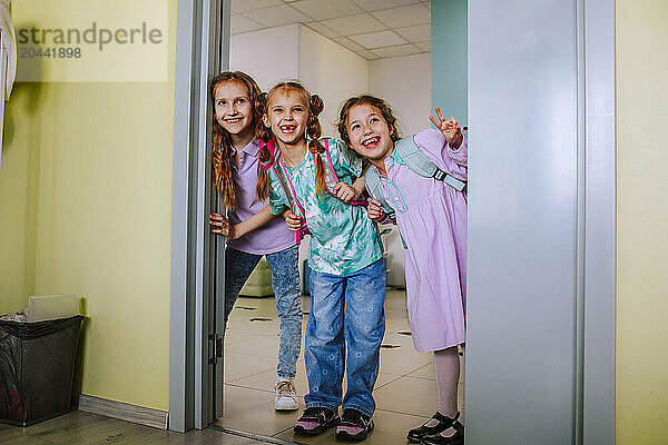 Happy school children gesturing standin in classroom door