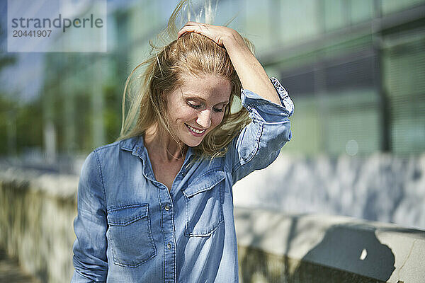 Smiling woman with hand in hair and standing near retaining wall