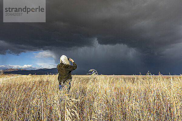 Rear view of woman taking photo of approaching storm with smart phone