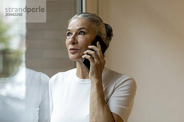 Senior woman talking on smart phone looking out through window