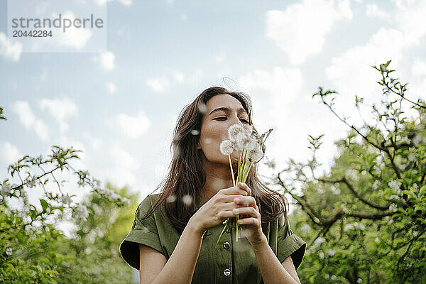 Woman blowing on dandelions under cloudy sky